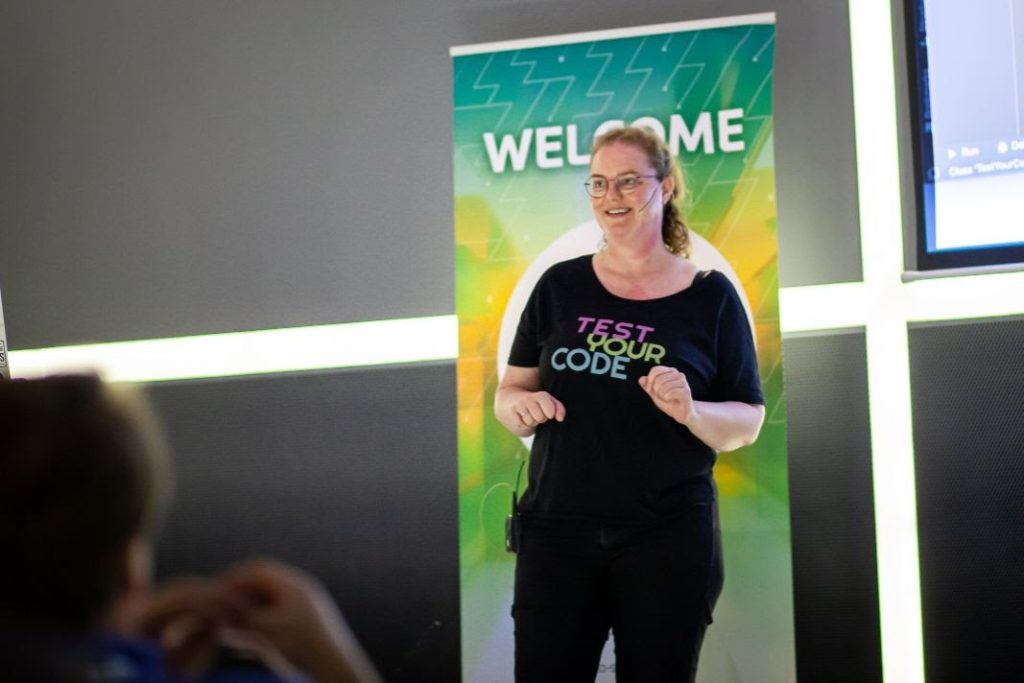 Marit van Dijk wearing a black t-shirt that says "Test your code"on stage speaking at JSpring