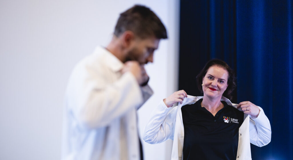 Piotr Przybył and Marit van Dijk simultaneously putting on their labcoat.