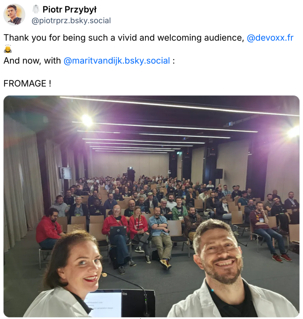 Social media post by Piotr Przybył with the text: "Thank you for being such a vivid and welcoming audience, Devoxx France. And now, with Marit van Dijk: FROMAGE !". The post contains a picture of Marit van Dijk and Piotr Przybył, both wearing labcoats, on stage at Devoxx France with the audience in the background.