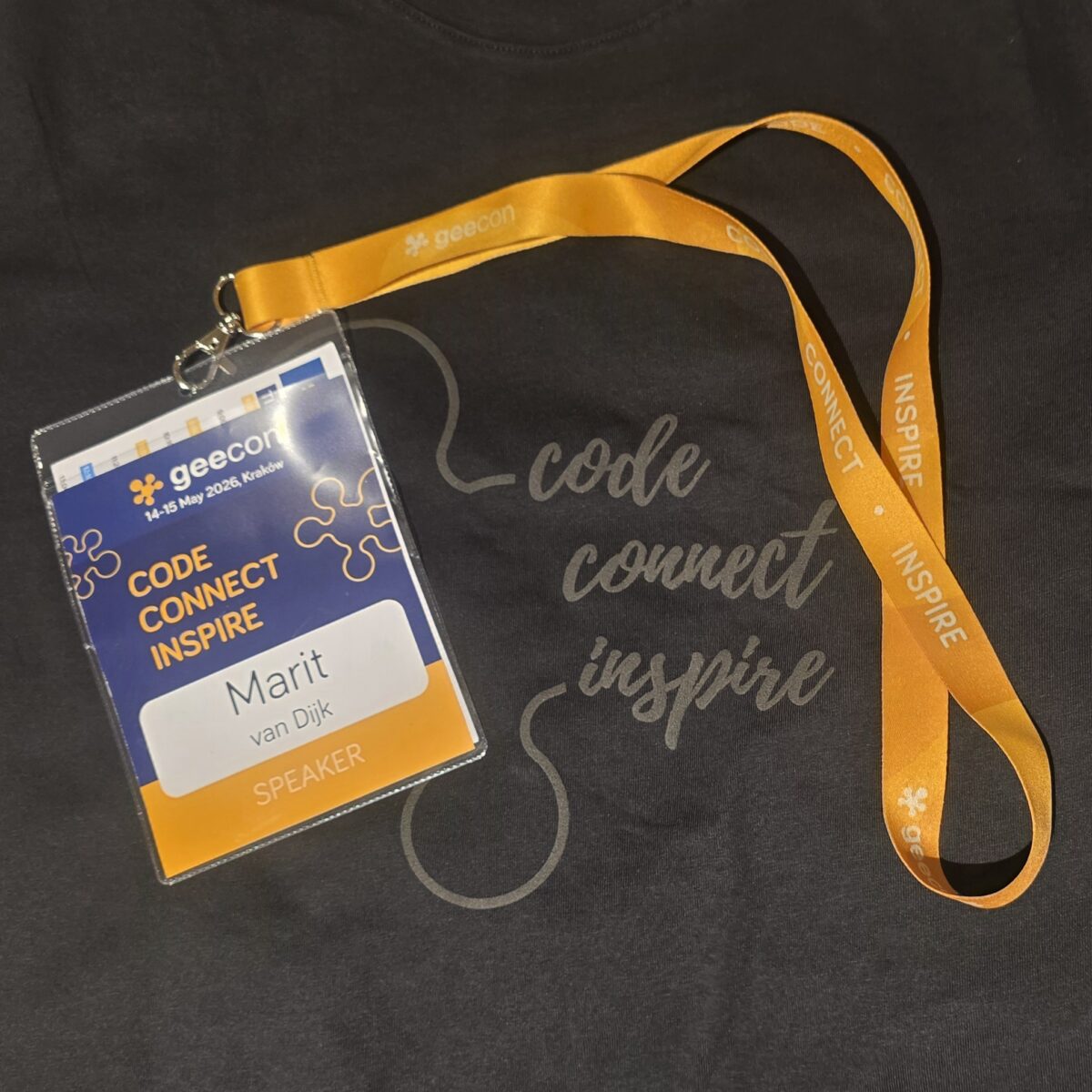 GeeCON speaker badge for Marit van Dijk on the black GeeCON 2026 t-shirt. Both badge and shirt have the GeeCON slogan: Code, connect, inspire.