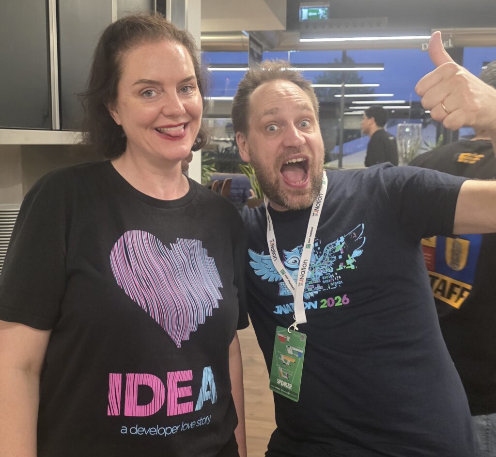 Marit van Dijk wearing a black IntelliJ IDEA t-shirt and and Sam Aaron wearing a dark blue JNation t-shirt. Marit is sticking out her tongue and Sam has his thumb up.