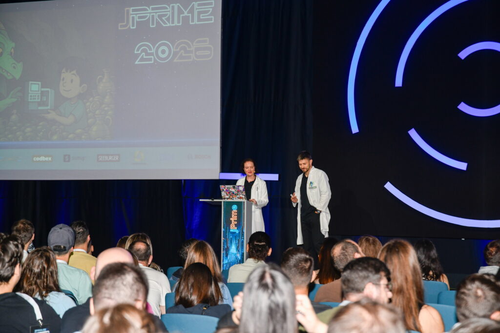 Marit van Dijk and Piotr Przybył speaking at jPrime; both are wearing a labcoat.